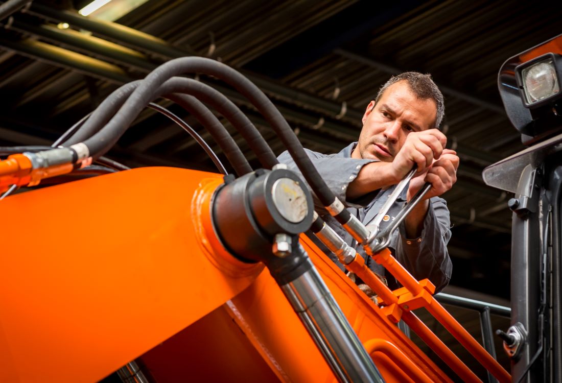 Man die sleutelt aan een arm van een oranje kraan